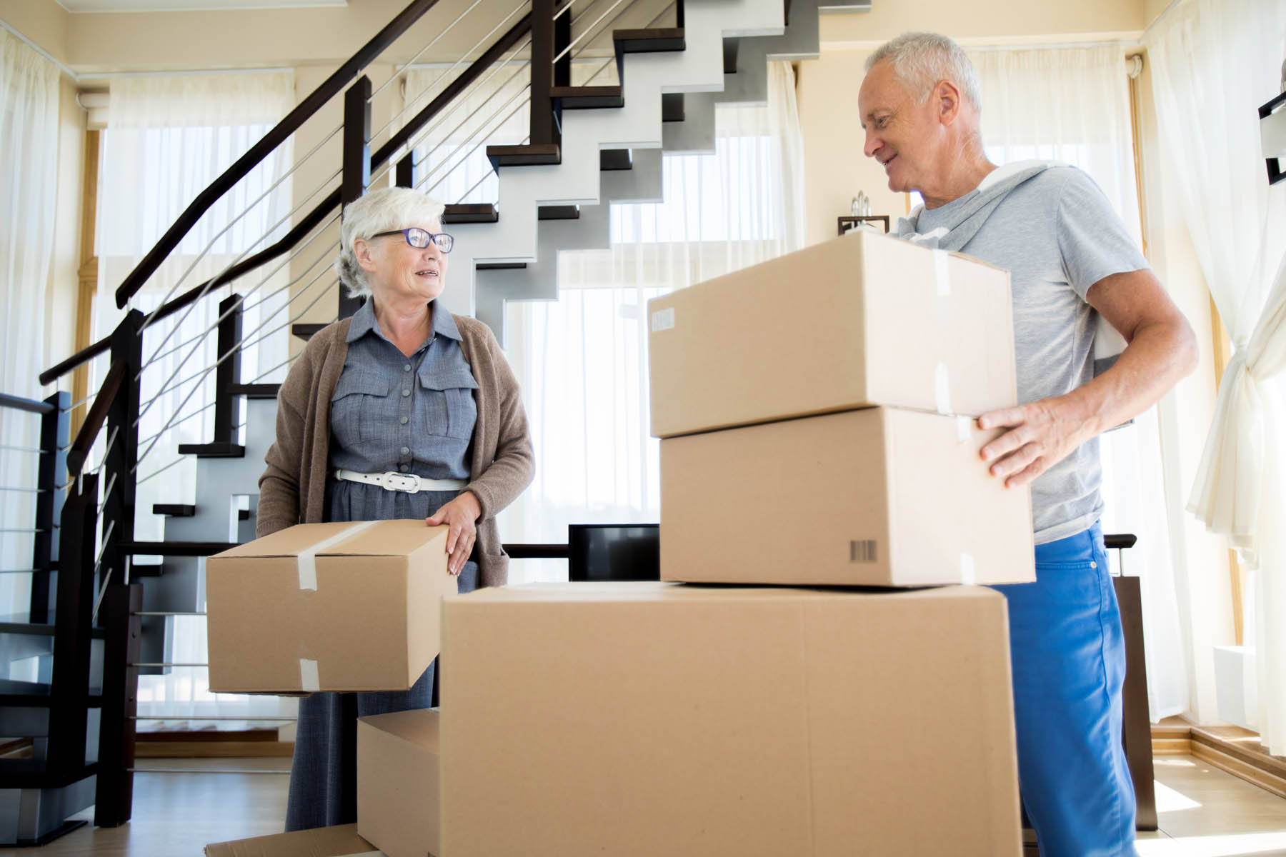 Portrait of happy senior couple packing cardboard boxes while moving to new house